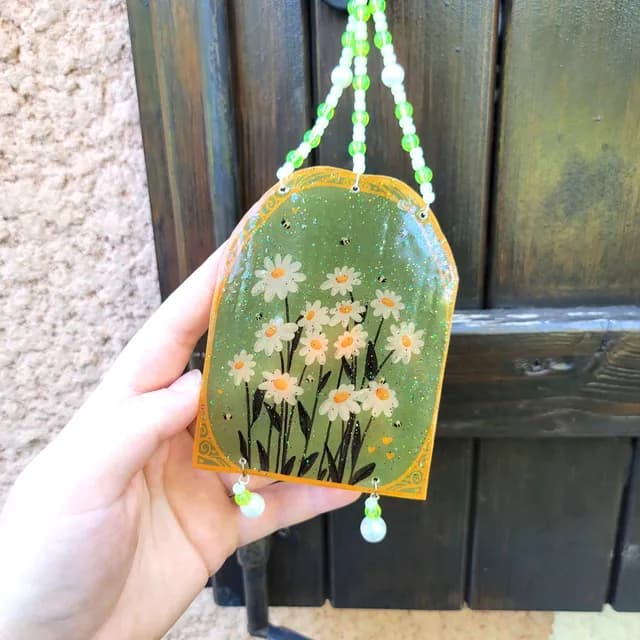 Suncatcher en forme d'arche illustré de pâquerettes sur fond vert pailleté avec perles blanches et vertes