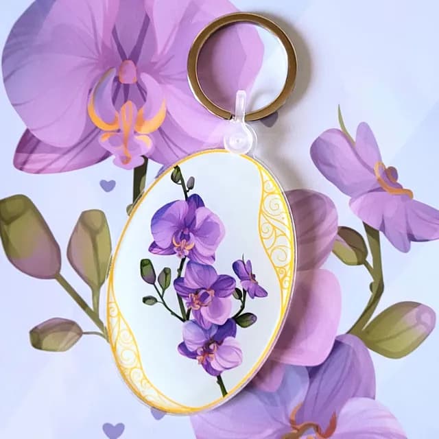 Porte-clés ovale illustré d'orchidées violettes avec liseré jaune doré sur fond floral assorti.