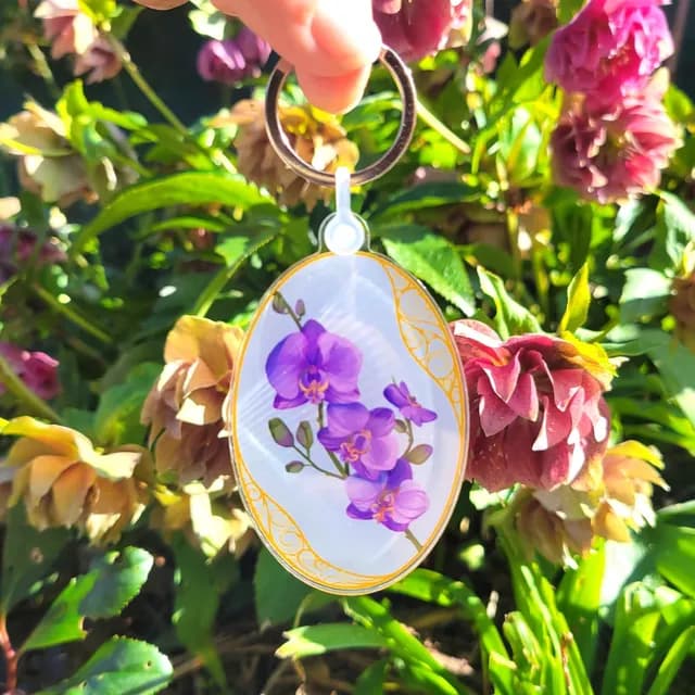 Détail du porte-clés en acrylique mettant en valeur le dessin d'orchidées violettes.