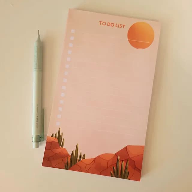 Bloc to-do list illustré d'un désert aux teintes ocre et saumon, posé à côté d'un porte-mine.