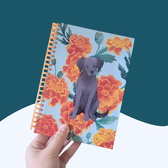 Carnet A5 tenu en main avec illustration d'un chien labrador parmi des fleurs orange et reliure spirale