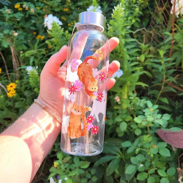 Gourde transparente tenue en main avec illustrations de chats roux et petites fleurs roses