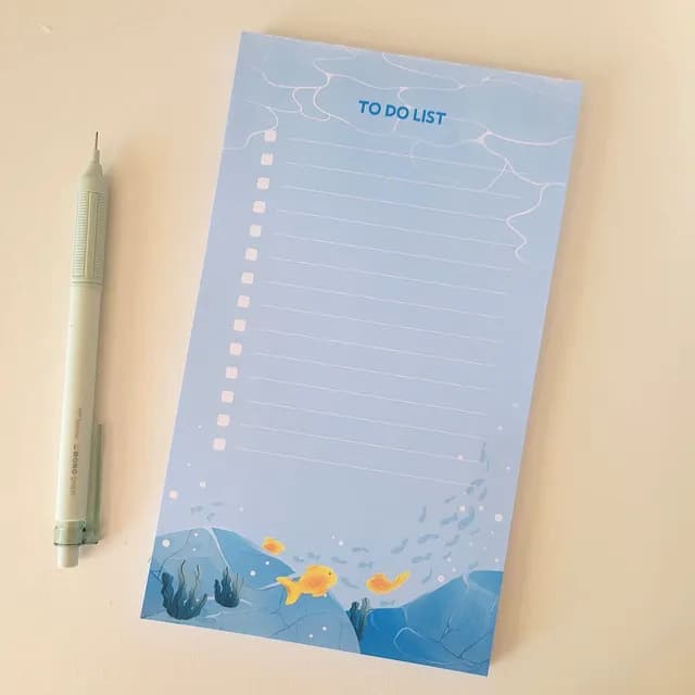 Bloc-notes to-do list bleu avec lignes, cases à cocher et décor de poissons marins, à côté d'un crayon.