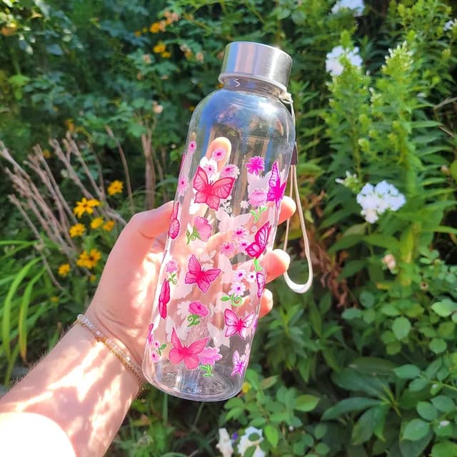 Gourde transparente tenue en main ornée de papillons et fleurs roses sur fond de jardin ensoleillé