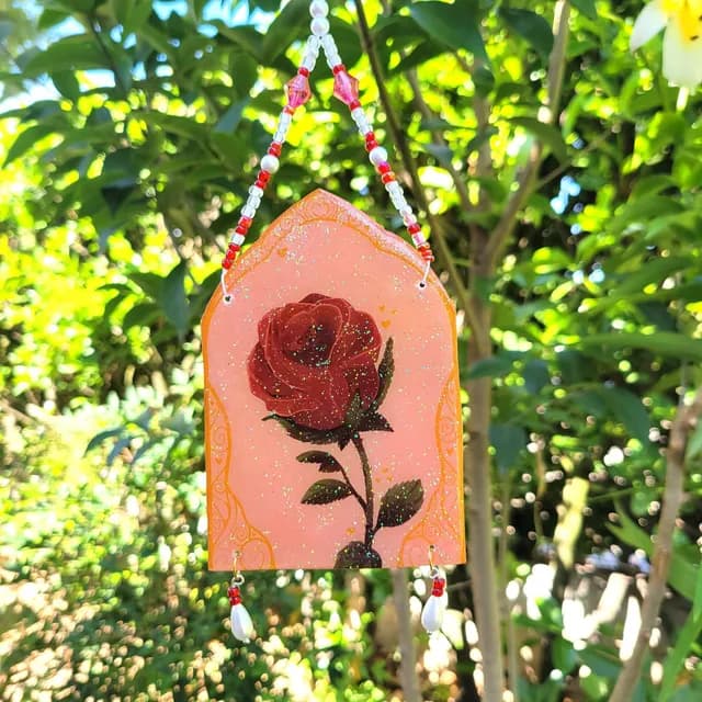 Suncatcher ogival orné d'une rose rouge pailletée suspendu à des perles blanches et rouges en extérieur