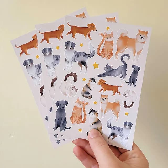 Détail des motifs illustrés de chats roux, chiens marron et petites étoiles jaunes sur la planche de stickers.
