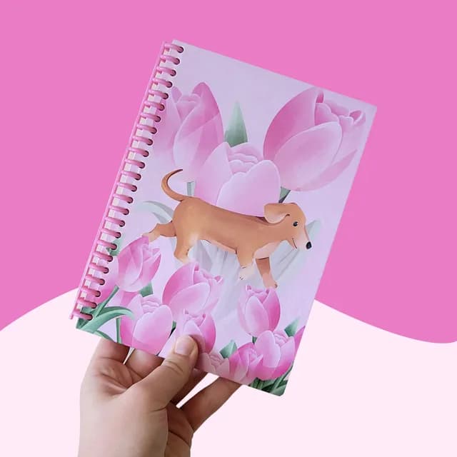 Main tenant un carnet à spirale rose orné d'un petit chien marron et de tulipes roses