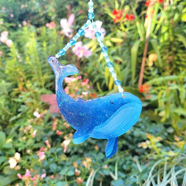 Suncatcher en forme de baleine bleue pailletée suspendu par une rangée de perles dans un jardin