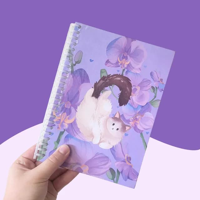 Carnet A5 à spirale tenu en main illustré d'un chat blanc au milieu d'orchidées violettes