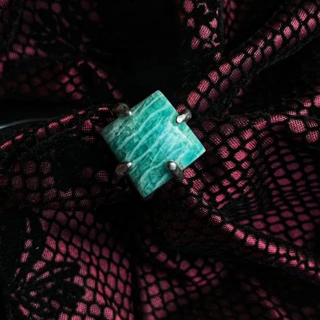 Bague en argent ornée d'une amazonite carrée vert clair veinée, posée sur de la dentelle noire ajourée.