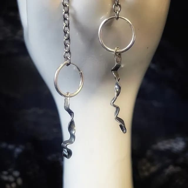 Paire de créoles en argent avec pendentifs ondulés façon ruban sur support blanc.