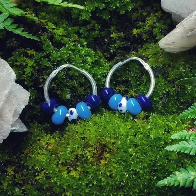 Paire de créoles en argent avec perles de verre bleues et blanches posées sur de la mousse naturelle.