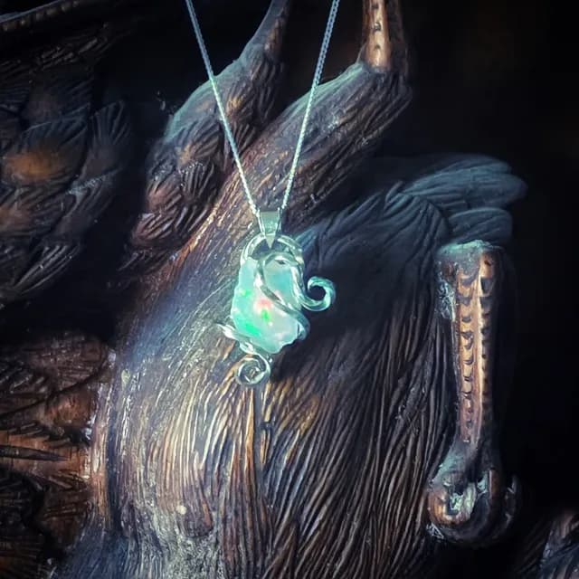 Pendentif en argent aux volutes travaillées sertissant une opale naturelle aux reflets irisés.