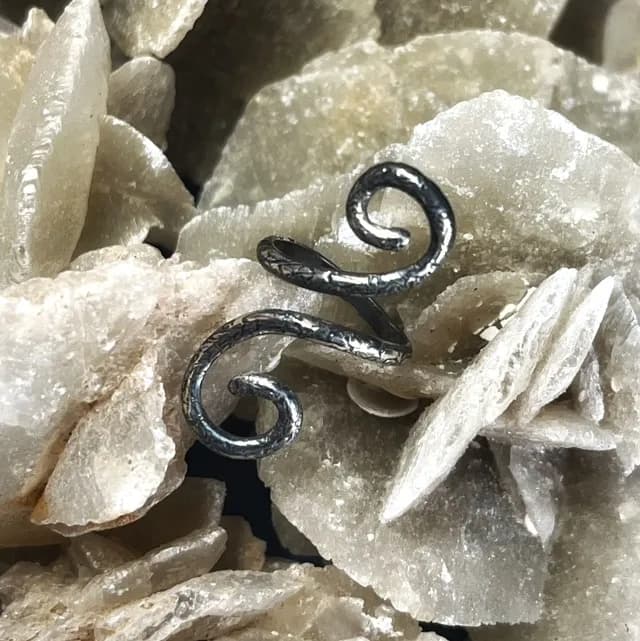 Bague de phalange en argent ornée de spirales texturées, posée sur une roche minérale beige.