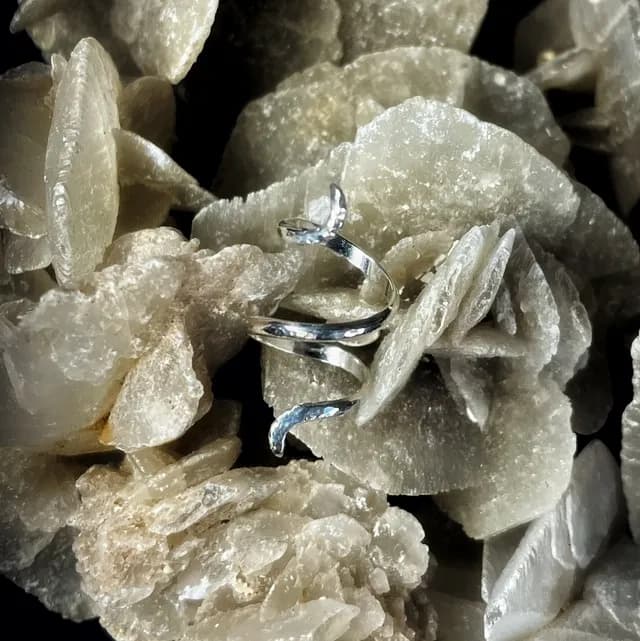 Bague de phalange en spirale en argent posée sur un cristal minéral beige
