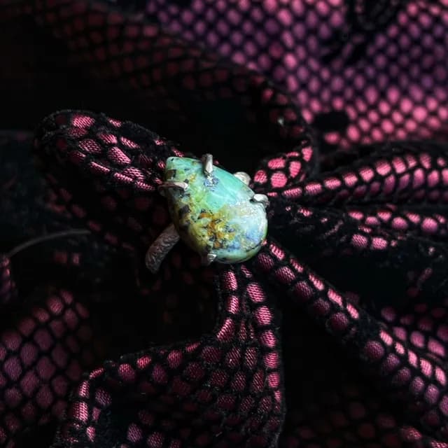 Bague en argent avec jaspe africaine verte en forme de goutte, posée sur un tissu texturé noir et rose.