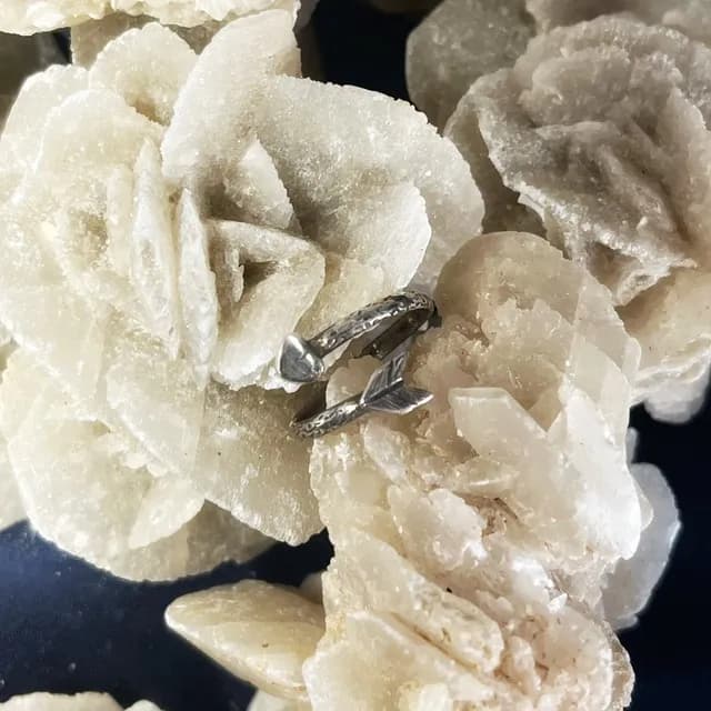 Bague Cupidon en argent en forme de flèche gravée, posée sur une roche minérale blanche.