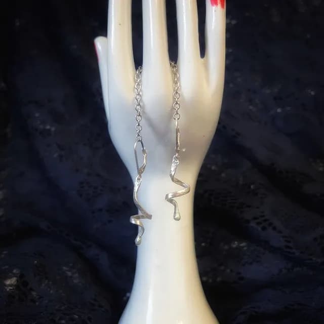 Paire de boucles d'oreilles en spirale argentée présentées sur une main en céramique blanche