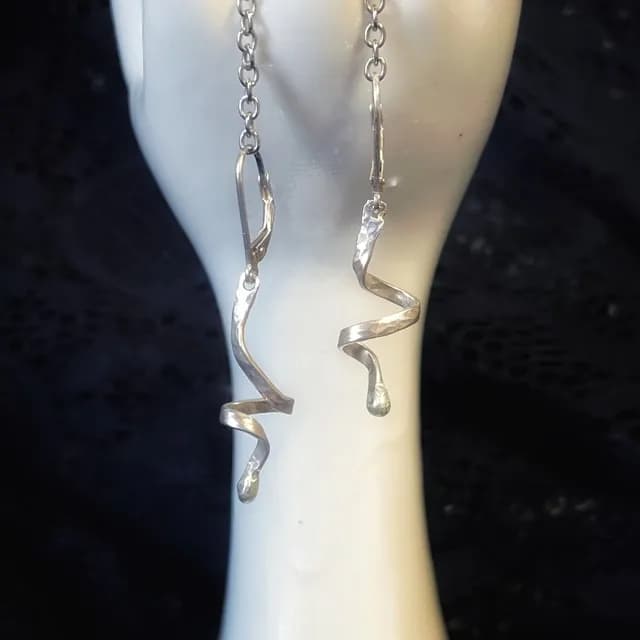 Gros plan sur deux boucles d'oreilles pendantes en spirale argentée suspendues à un support blanc