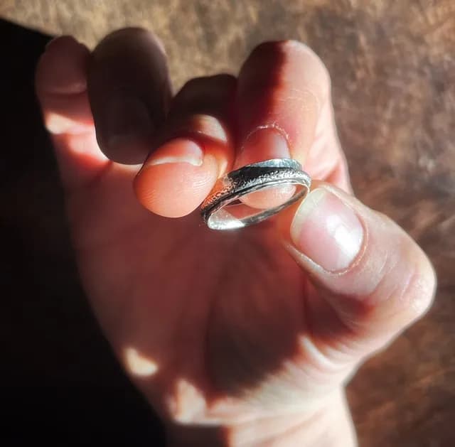 Bague argentée martelée avec anneau mobile tenue entre les doigts d'une main.