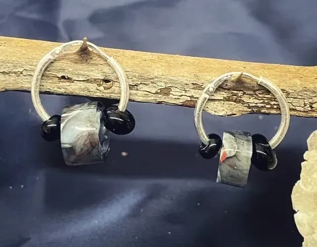 Paire de créoles en argent ornées de perles cylindriques marbrées et de petites perles noires sur bois flotté.