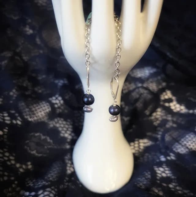 Boucles d'oreilles pendantes en argent avec perles sombres irisées, sur un présentoir main.