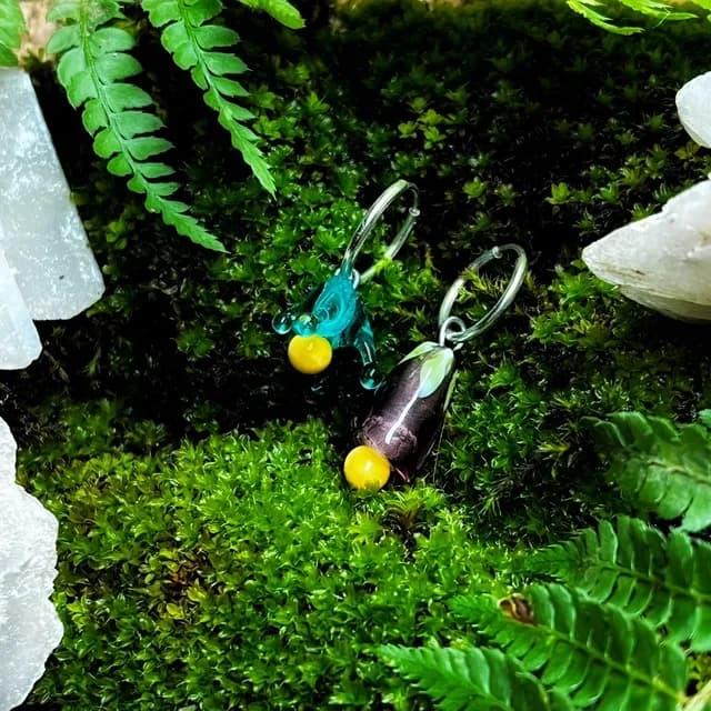 Créoles en argent et perles pendantes en verre sculpté bleu, sombre et jaune sur un lit de mousse verte