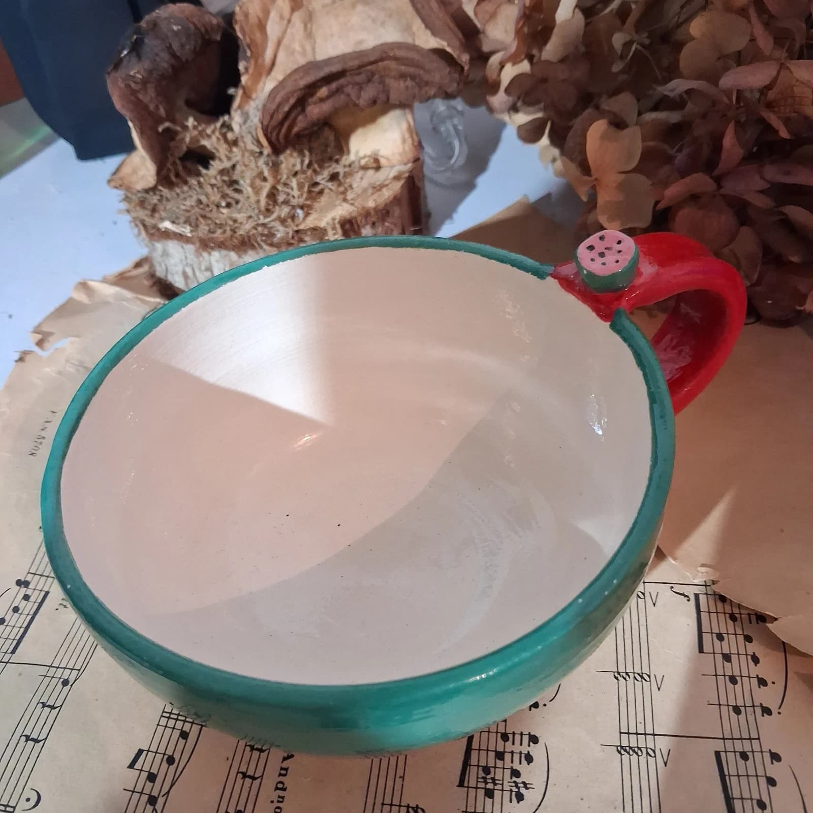 Tasse bol verte en céramique vue du dessus avec anse rouge ornée d'une pastèque miniature.