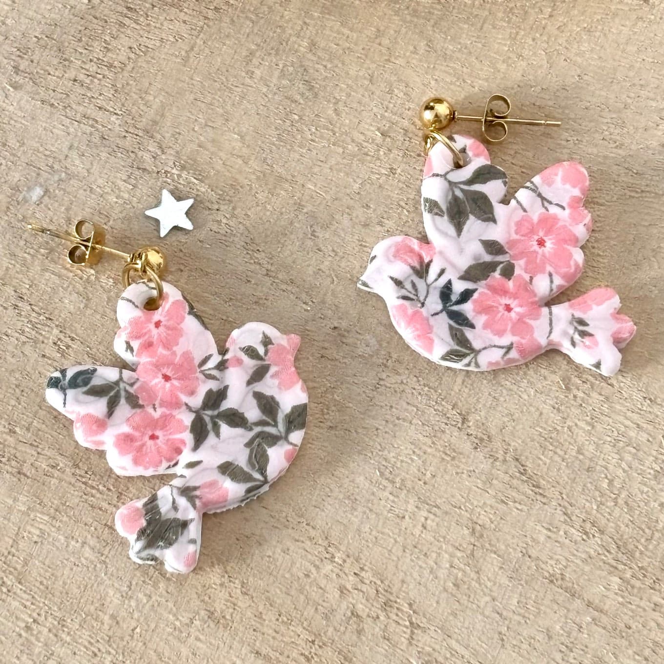 Boucles pendantes en forme d'oiseaux à motif de fleurs roses sur fond de bois clair