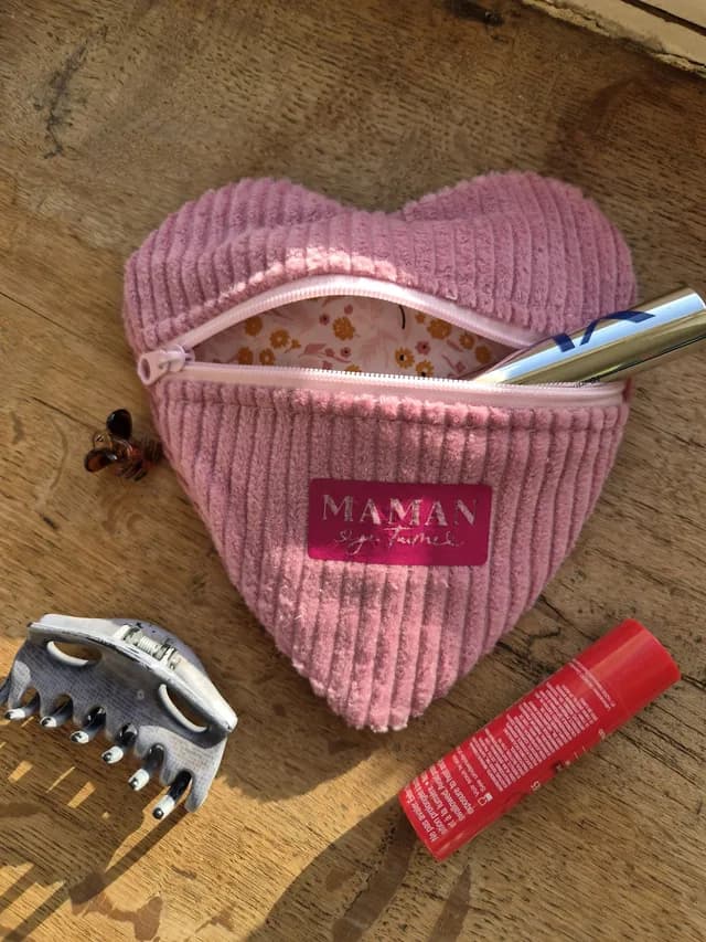 Pochette cœur en velours côtelé rose Maman je t'aime ouverte avec maquillage et pinces sur une table.