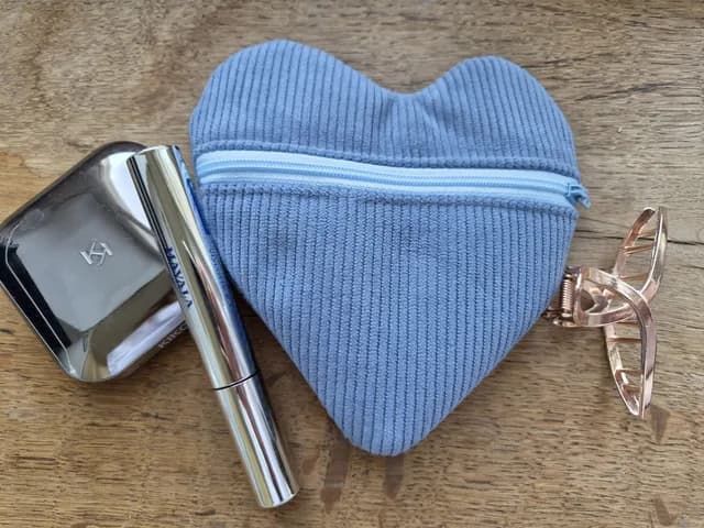 Pochette cœur en velours bleu ciel ouverte, révélant une doublure à fleurs bleues et des accessoires.