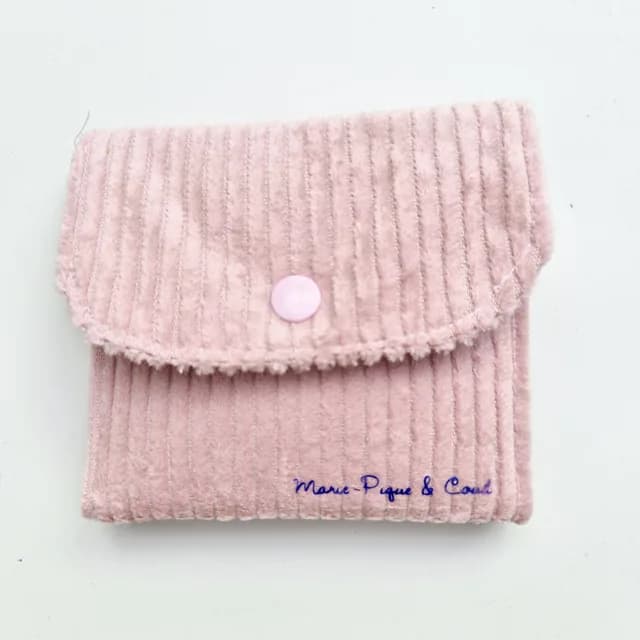 Pochette fermée rose poudré à texture côtelée avec rabat à bouton pression sur fond blanc.