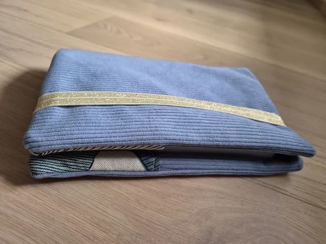 Pochette à livre fermée en velours côtelé bleu avec élastique doré pailleté sur parquet en bois.