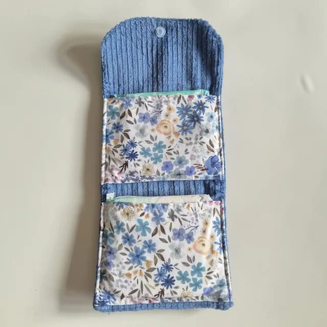 Pochette ouverte en velours côtelé bleu, doublure fleurie et compartiments de rangement.