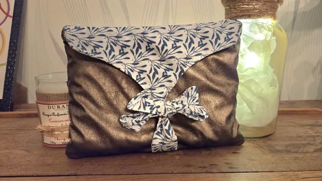 Pochette livre bronze fermée par un ruban noué à motif végétal bleu et blanc