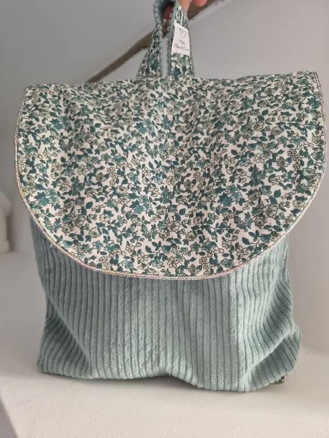 Sac à dos maternelle en velours côtelé vert d'eau avec rabat fleuri bordé de passepoil scintillant.