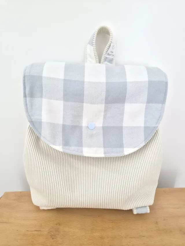 Sac à dos enfant en velours côtelé crème avec rabat en flanelle à carreaux blanc et gris clair.