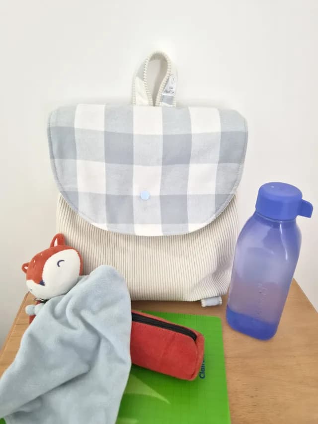 Dos du sac à dos d'école crème montrant les bretelles réglables et la poignée de suspension.