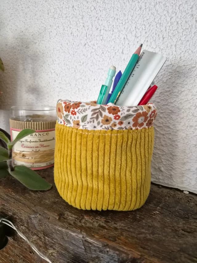 Pot à crayons en velours côtelé jaune et tissu à fleurs, rempli de fournitures sur une poutre.