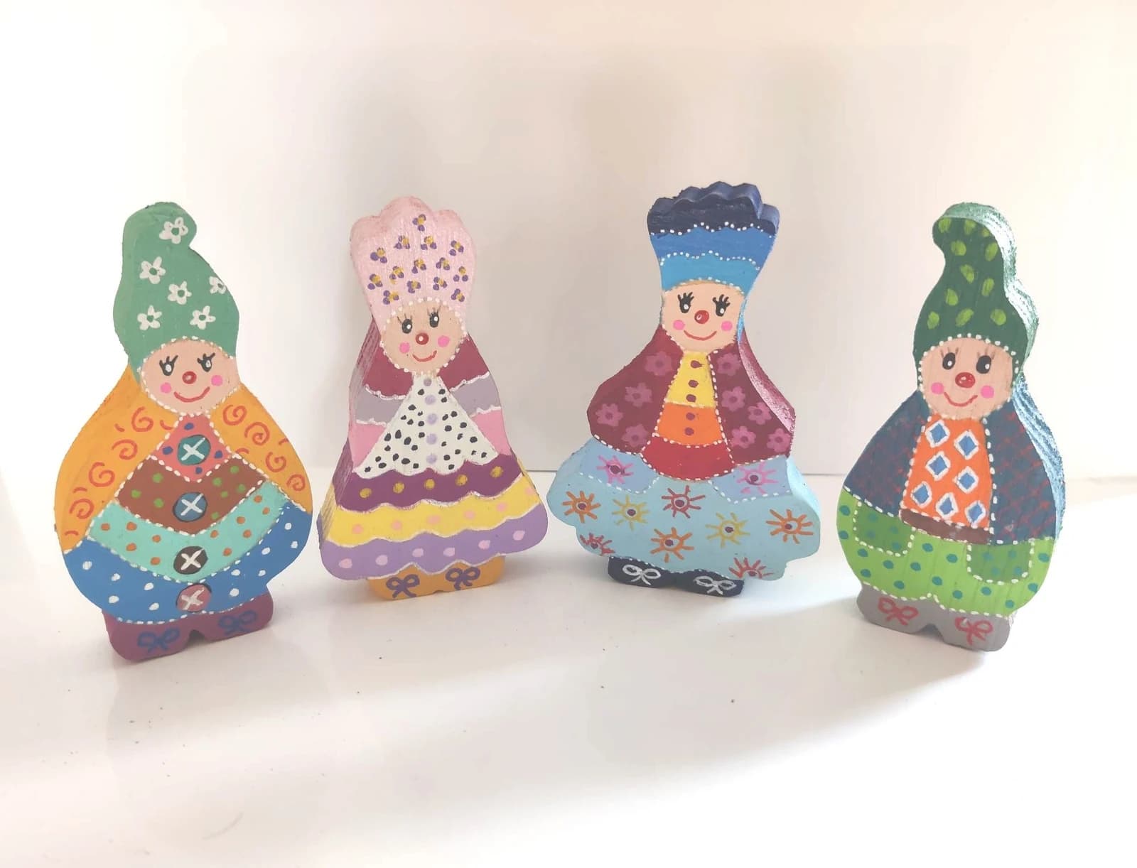 Quatre figurines lutins Farfs en bois peints à la main aux couleurs vives sur fond blanc.