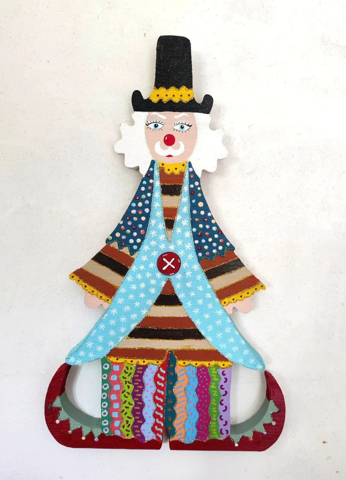 Grand clown décoratif mural en bois peint avec habit bleu étoilé, pantalon rayé multicolore et chapeau noir.