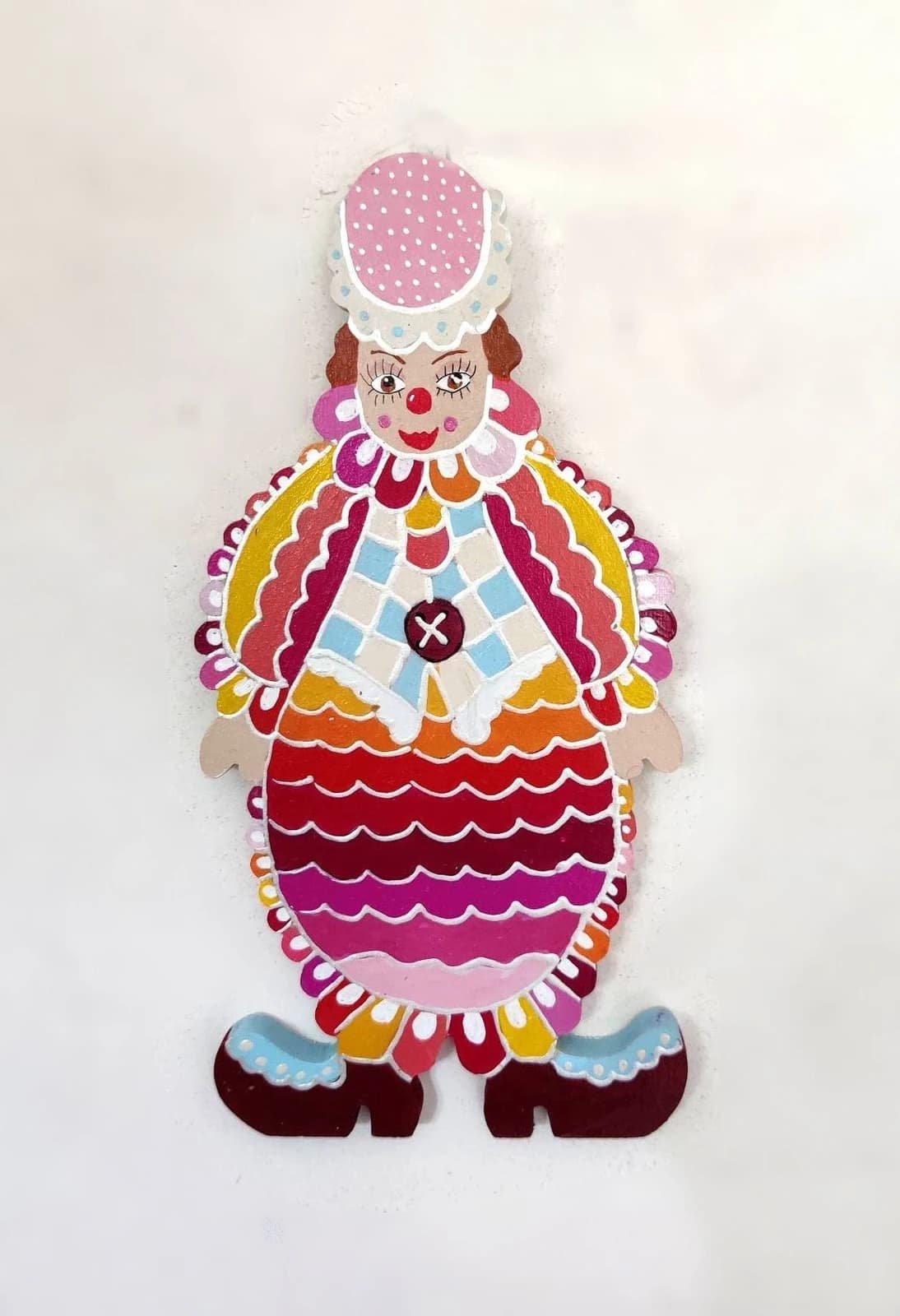 Clown mural en bois peint aux motifs ondulés roses, rouges et orange avec chapeau rose à pois.