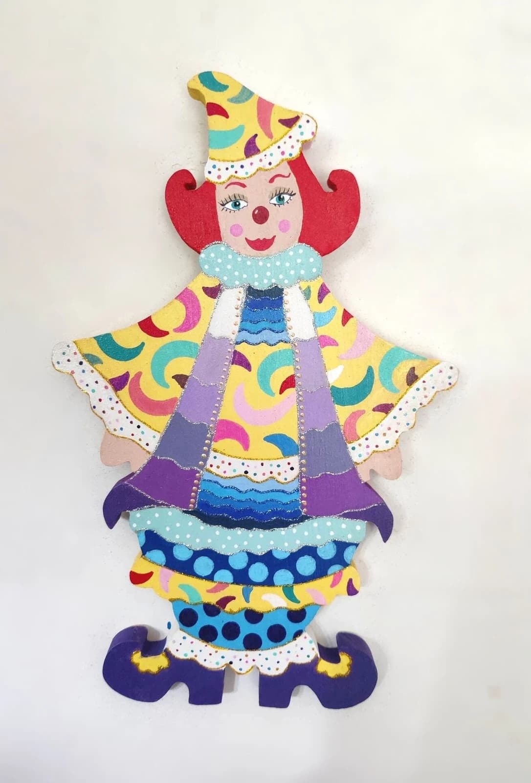 Clown mural en bois découpé et peint de motifs colorés jaunes, violets et bleus avec cheveux rouges.