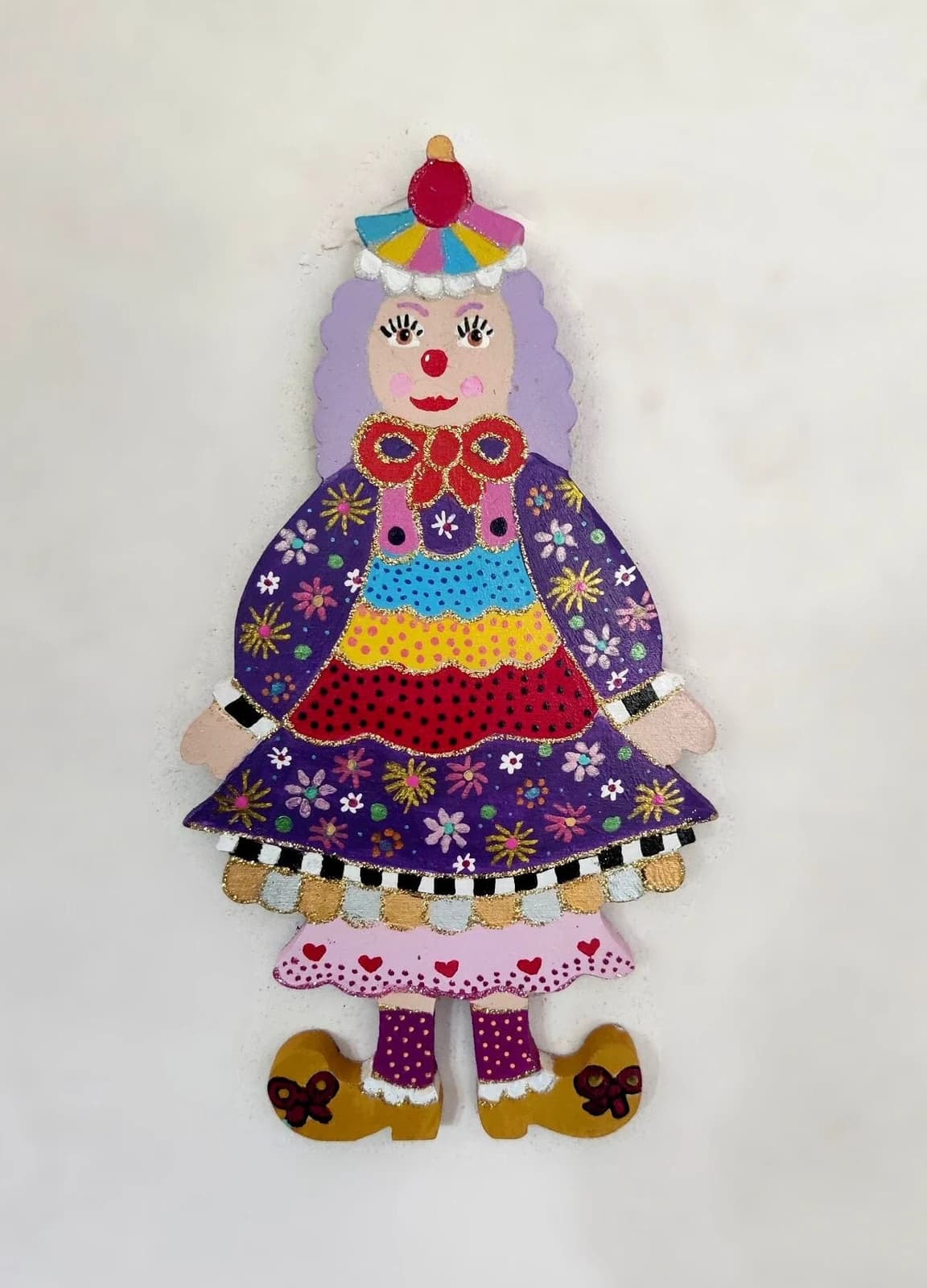 Figurine de clown en bois Violetta aux cheveux mauves et robe violette fleurie peinte de détails colorés.