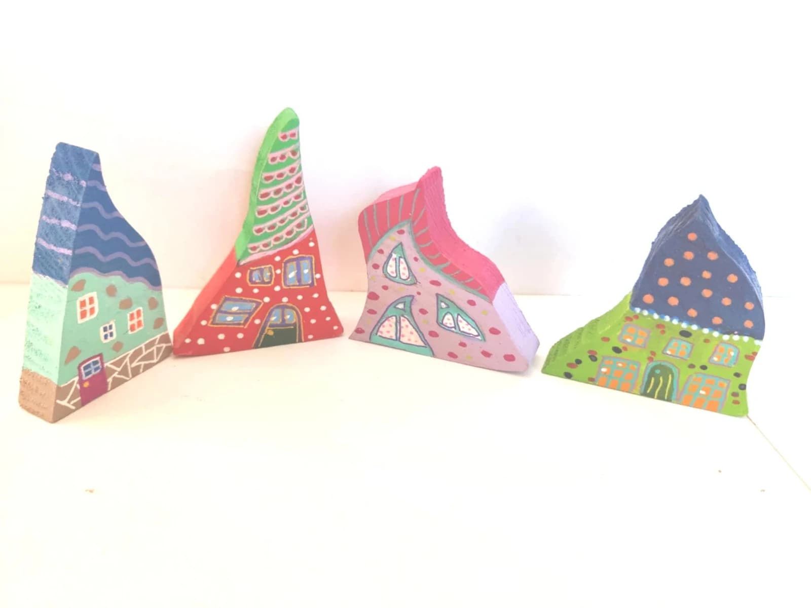 Quatre maisonnettes miniatures colorées en bois aux toits asymétriques peints sur fond blanc