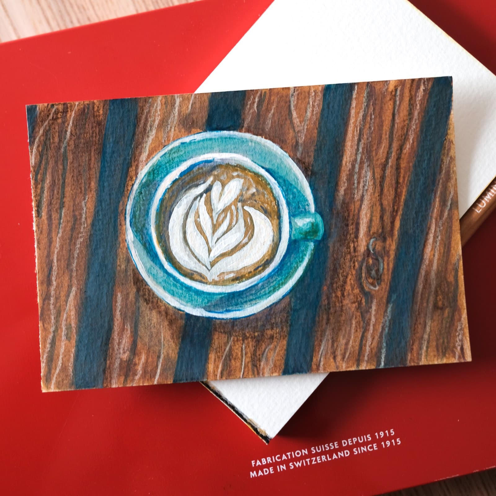 Peinture petit format d'une tasse turquoise vue du dessus avec latte art sur fond effet bois
