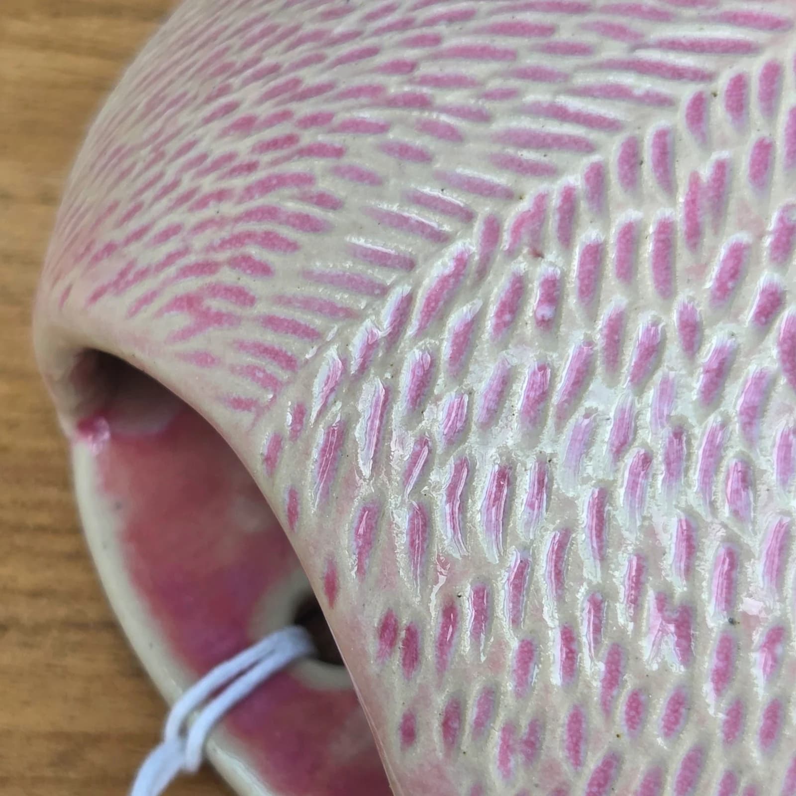 Détail de la texture gravée et des nuances rose poudré du petit vase mural rond en céramique.