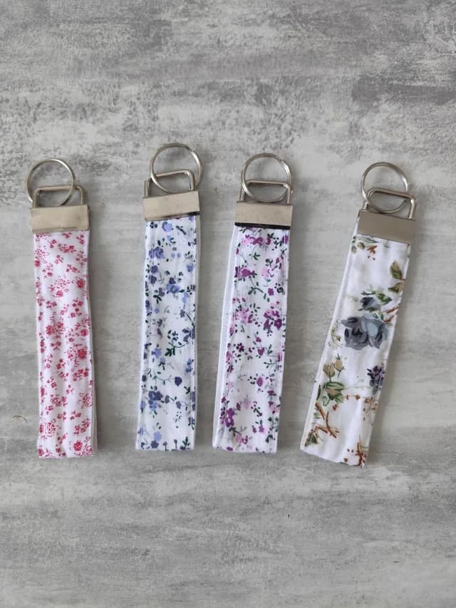 Quatre porte-clés en ruban de tissu aux motifs floraux rouge, bleu, violet et beige avec anneaux métalliques
