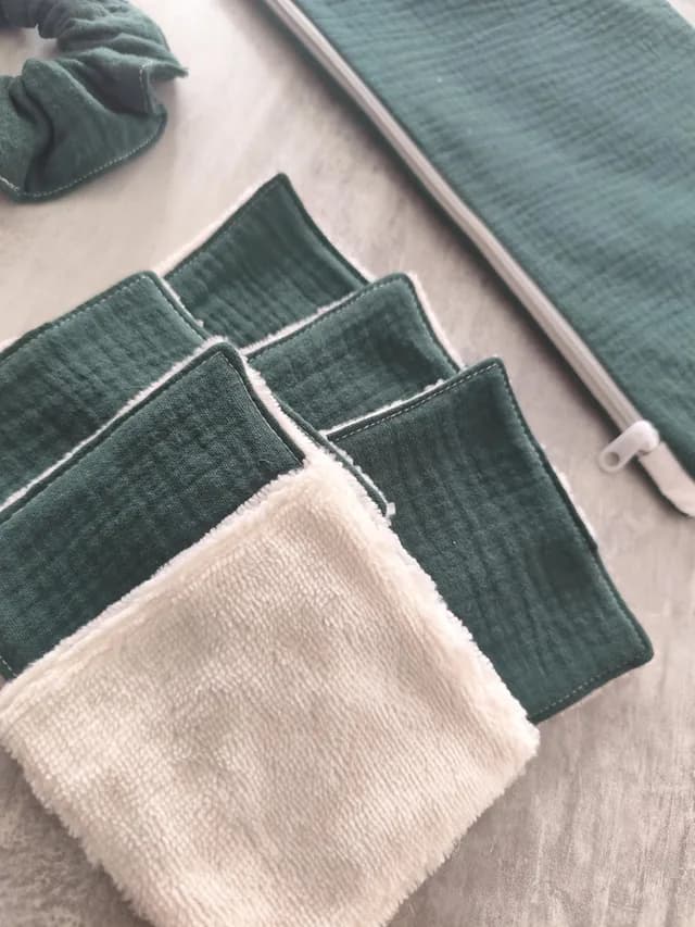 Détail des lingettes lavables vert foncé doublées de tissu doux blanc à côté de la pochette.