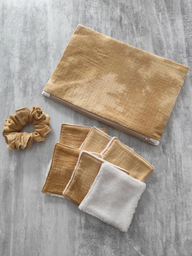 Pochette zippée ocre, chouchou assorti et lingettes lavables carrées disposés sur un fond gris.